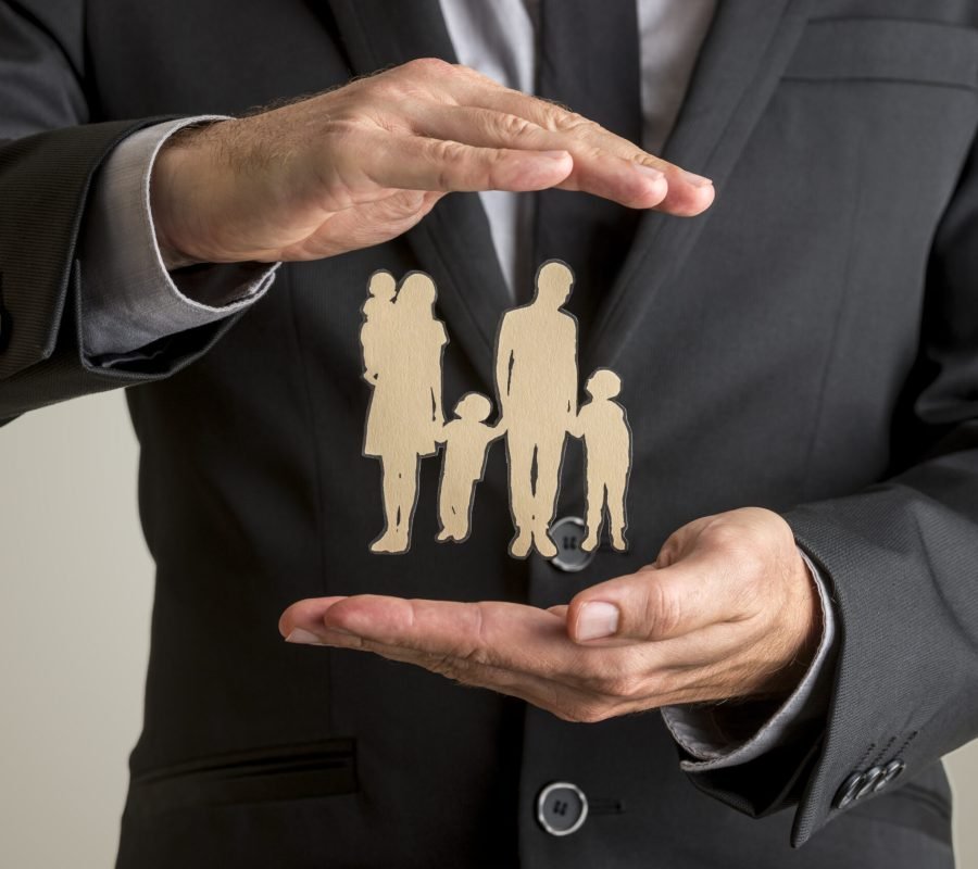 Businessman protecting family silhouette with a father, mother, baby and two children with his cupped hands in conceptual image of life insurance and security.
